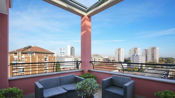 A balcony with wicker furniture and potted plants, overlooking a cityscape with high-rise buildings. - Milano Certosa Apartment (Milano)