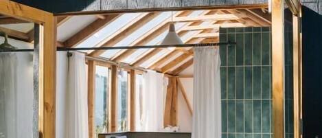 A wooden deck leading to a bathroom with a shower and sink, under a sloped roof with wooden beams.