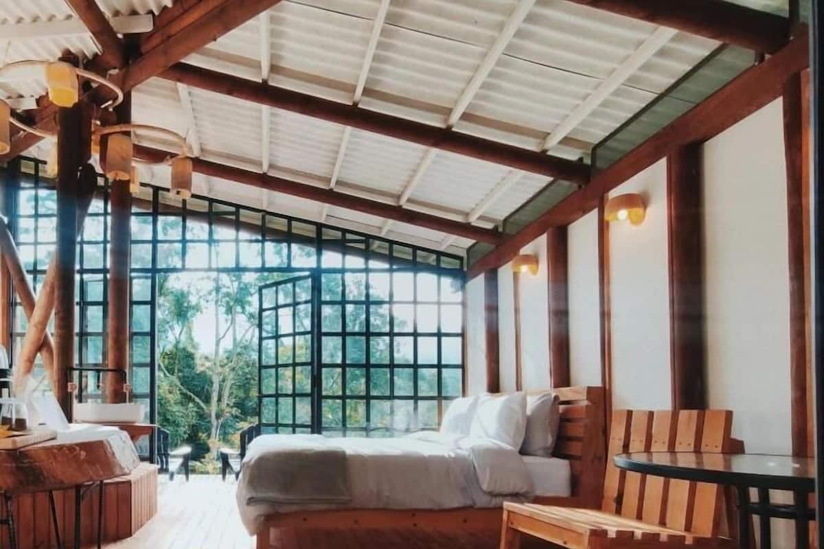 A spacious room with a large bed, wooden furniture, and large windows offering a view of the outdoors.