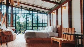 A spacious room with a large bed, wooden furniture, and large windows offering a view of the outdoors.