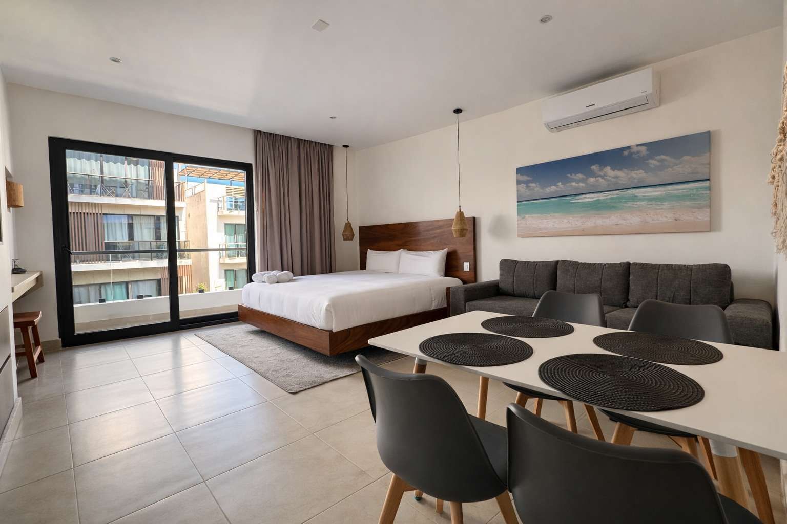 Una habitación de hotel moderna con cama, sofá, mesa de comedor con sillas y un balcón con vistas a edificios.
