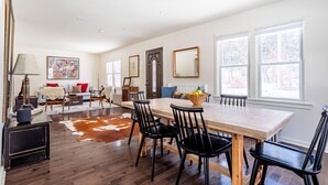 A spacious living room with a large wooden dining table, black chairs, and a cowhide rug. - NEW: In-town home w/ gorgeous cedar sauna+fire-pit (Livingston Manor)