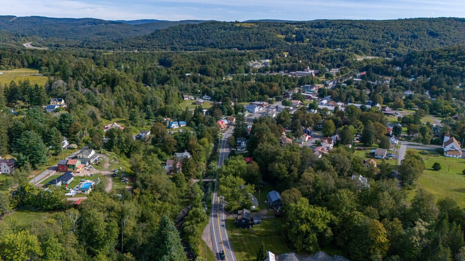 An aerial view of a small town with houses, roads, and surrounding forested hills.