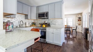 A modern kitchen with grey cabinets, a stainless steel microwave, and a large island with bar stools. - NEW: In-town home w/ gorgeous cedar sauna+fire-pit (Livingston Manor)