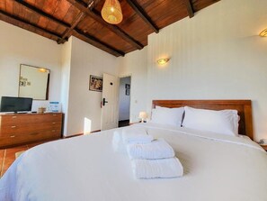 A hotel room with a large bed, wooden headboard, white linens, a wooden dresser, a television, and a mirror. - Torre de Santiago Guest House (Caminha)