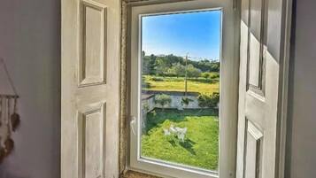 Una habitación con ventana que da a un espacio exterior con césped, una valla blanca y algunas sillas blancas.