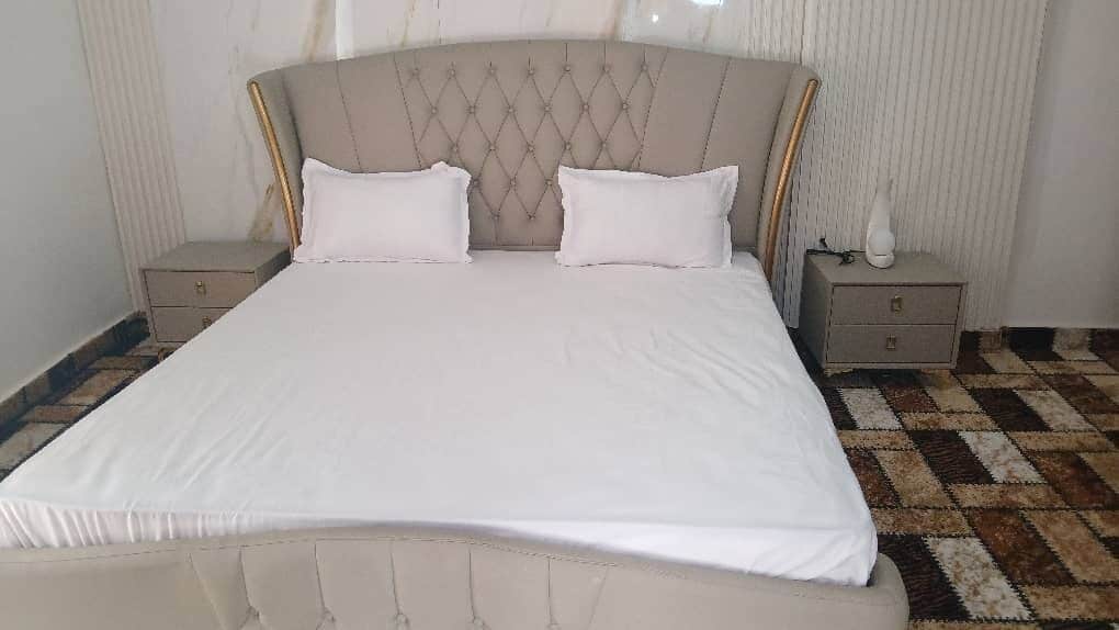 A bed with a tufted headboard, two bedside tables, and a patterned floor.