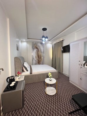 Une chambre d’hôtel comprenant un lit, une table de chevet, une petite table ronde avec un vase, une armoire et un téléviseur fixé au mur.