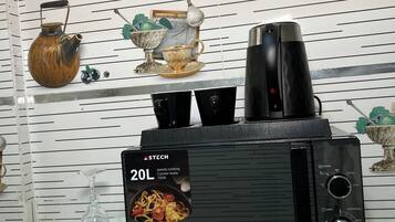 Ett kök med en svart kaffebryggare, en 20-liters mikrovågsugn för snabb matlagning och dekorativa föremål på väggen.