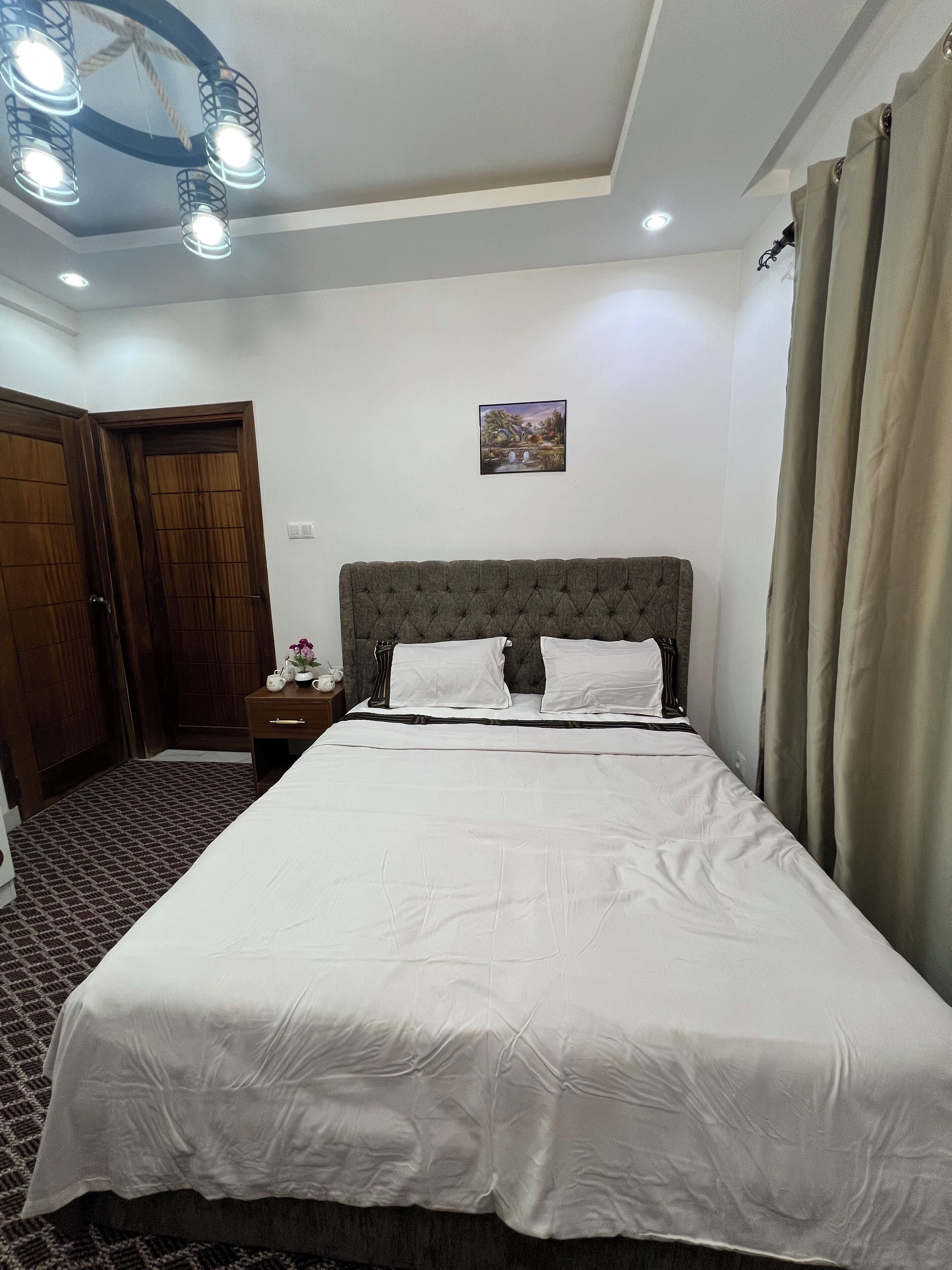 Une chambre à coucher bien rangée, avec un grand lit, une porte en bois, une petite table de chevet et un luminaire au plafond.