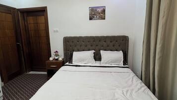 Une chambre à coucher bien rangée, avec un grand lit, une porte en bois, une petite table de chevet et un luminaire au plafond.