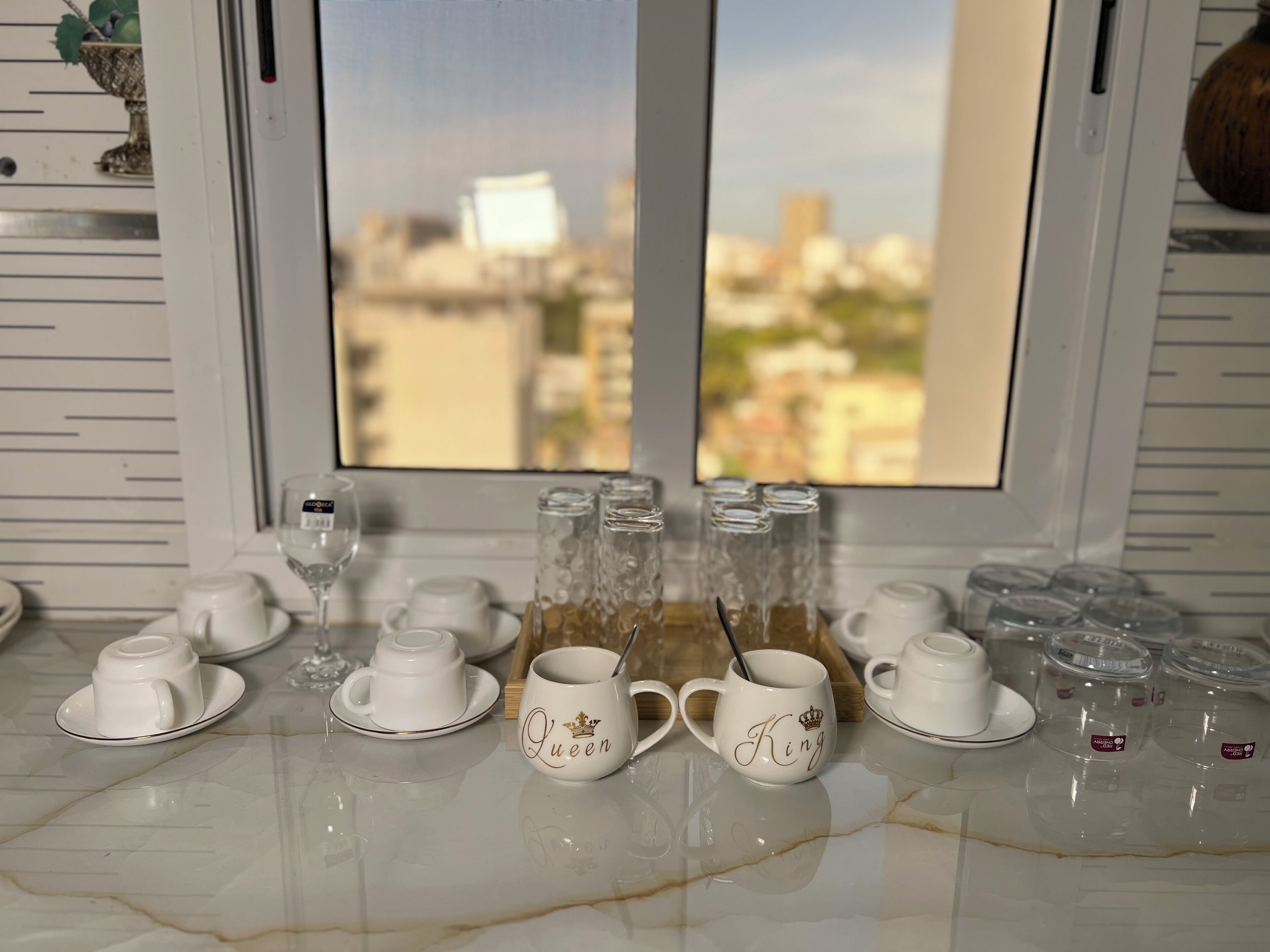 Uma bancada de cozinha com xícaras e pireses de cerâmica brancos, uma cafeteira e saleiro e pimenteiro.
