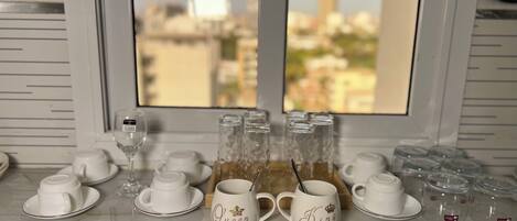 Uma bancada de cozinha com xícaras e pireses de cerâmica brancos, uma cafeteira e saleiro e pimenteiro.