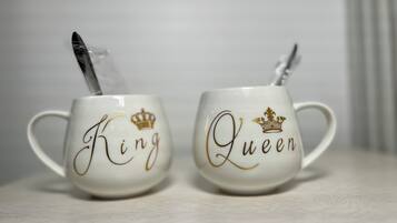 Twee witte keramische mokken met gouden letters en kroonmotieven, waarop 'King' en 'Queen' staan.