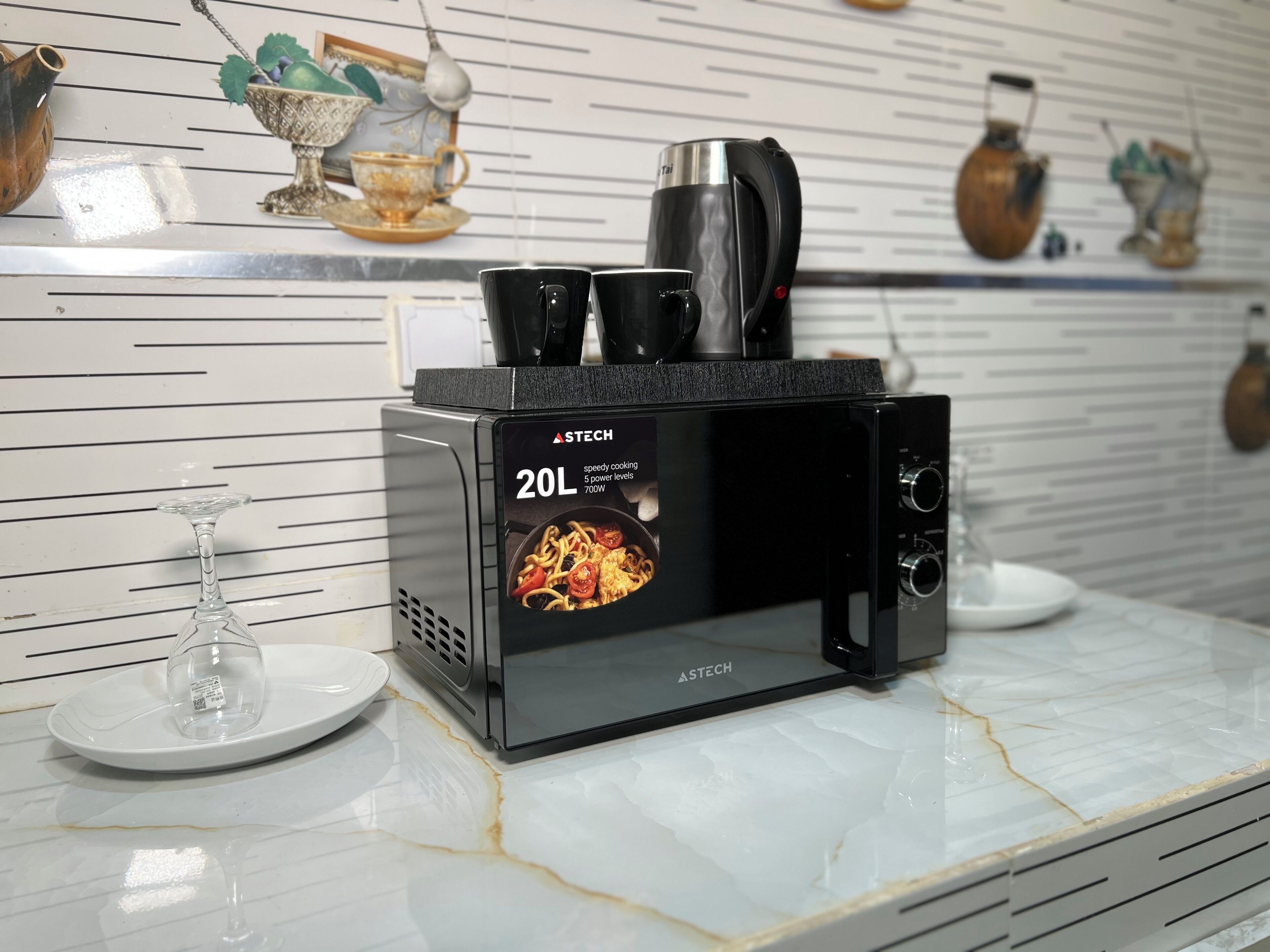 Une cuisine avec un four à micro-ondes posé sur un plan de travail en marbre, un verre à vin et des objets décoratifs accrochés au mur.