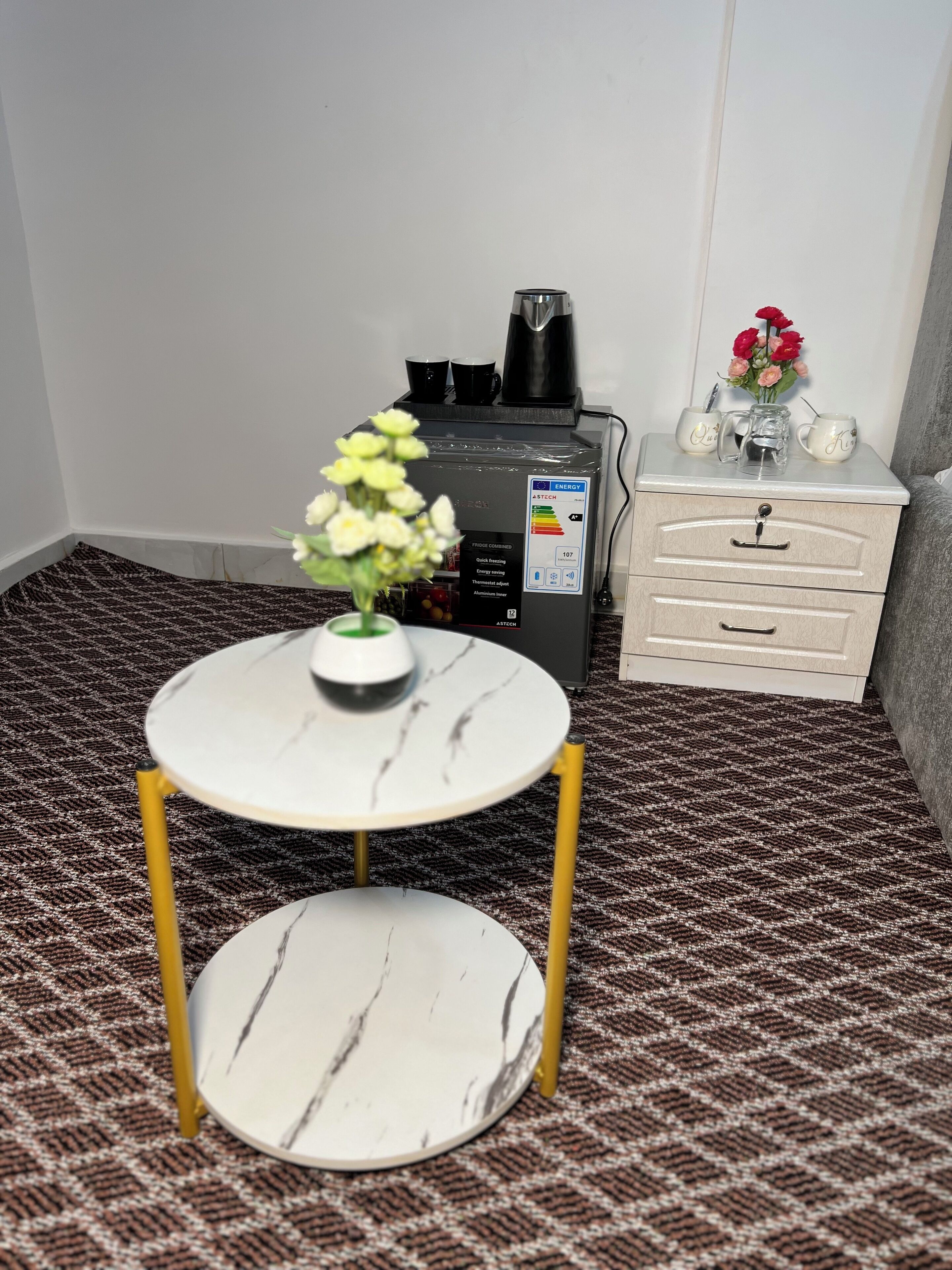 Una habitación pequeña con una mesa de mármol blanco, una cómoda blanca y una cafetera sobre una encimera blanca.