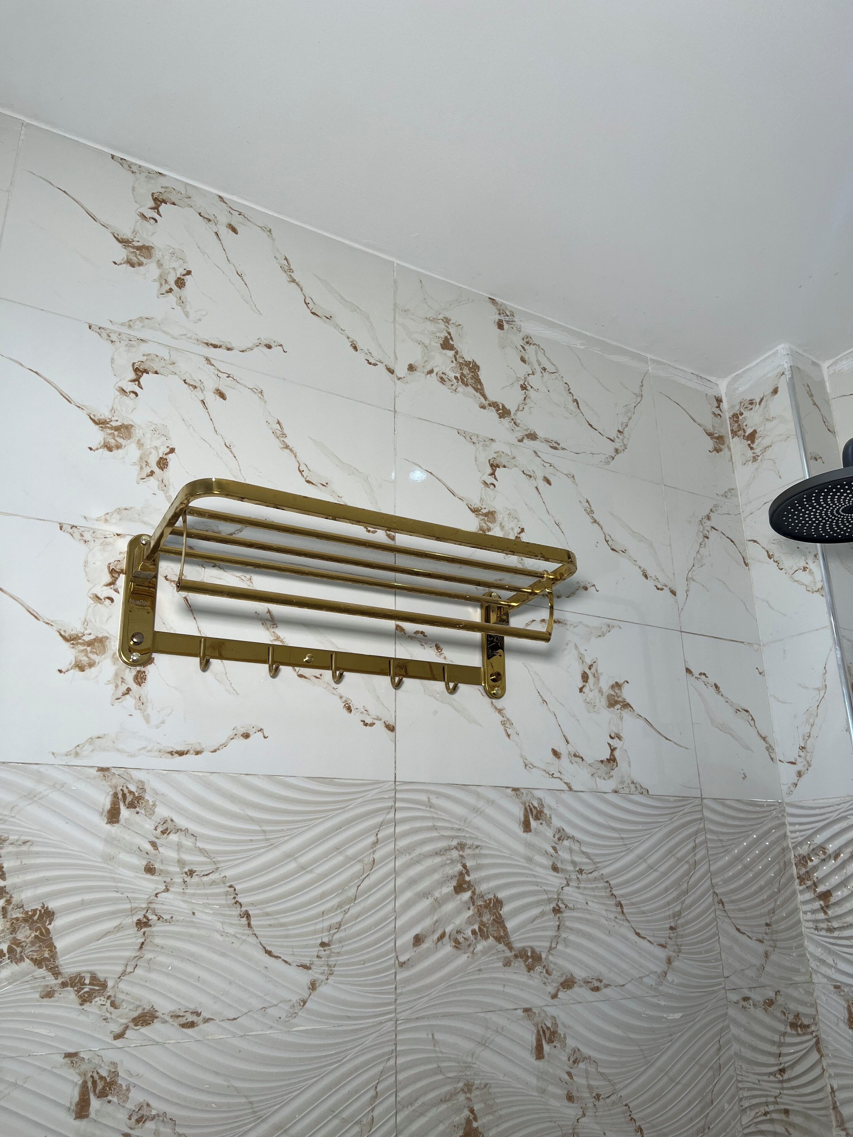 A bathroom with marble walls, a gold towel rack, and a shower head.