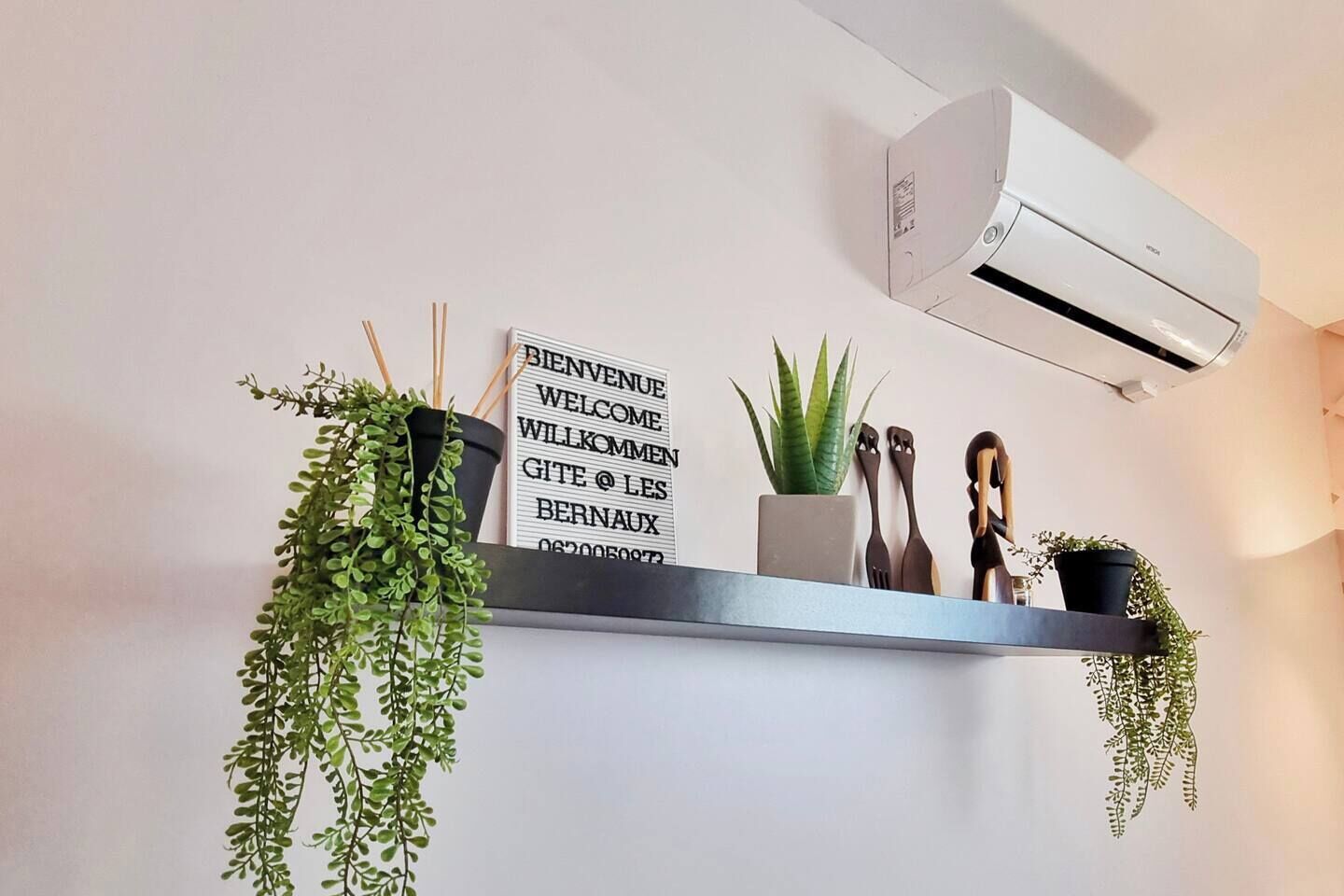 Una cuina moderna amb aire condicionat fixat a la paret, un cartell de benvinguda i diverses plantes en testos.