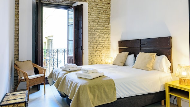 A bedroom with a large bed, a wicker chair, a wooden nightstand, and a stone wall. - Elegant pet-friendly family home in Santa Cruz, near the Cathedral (Sevilla)