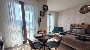 Ein modernes Schlafzimmer mit Bett, Esstisch und Stühlen sowie einer Aussicht ins Freie durch große Fenster.