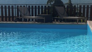 Ein Schwimmbad mit klarem Wasser, umgeben von einer Holzterrasse mit Stühlen und einem Tisch.