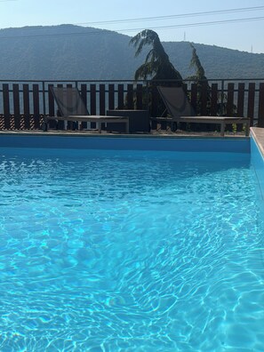 Una piscina con agua cristalina, rodeada por una terraza de madera con sillas y una mesa.