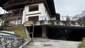 Ein mehrstöckiges Gebäude mit einem geneigten Dach, Balkonen und einer Treppe, die zum Eingang führt.