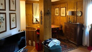 Ein Holzinnenraum mit Fernseher, gerahmten Pflanzenbildern, einer Essecke und einer Treppe.