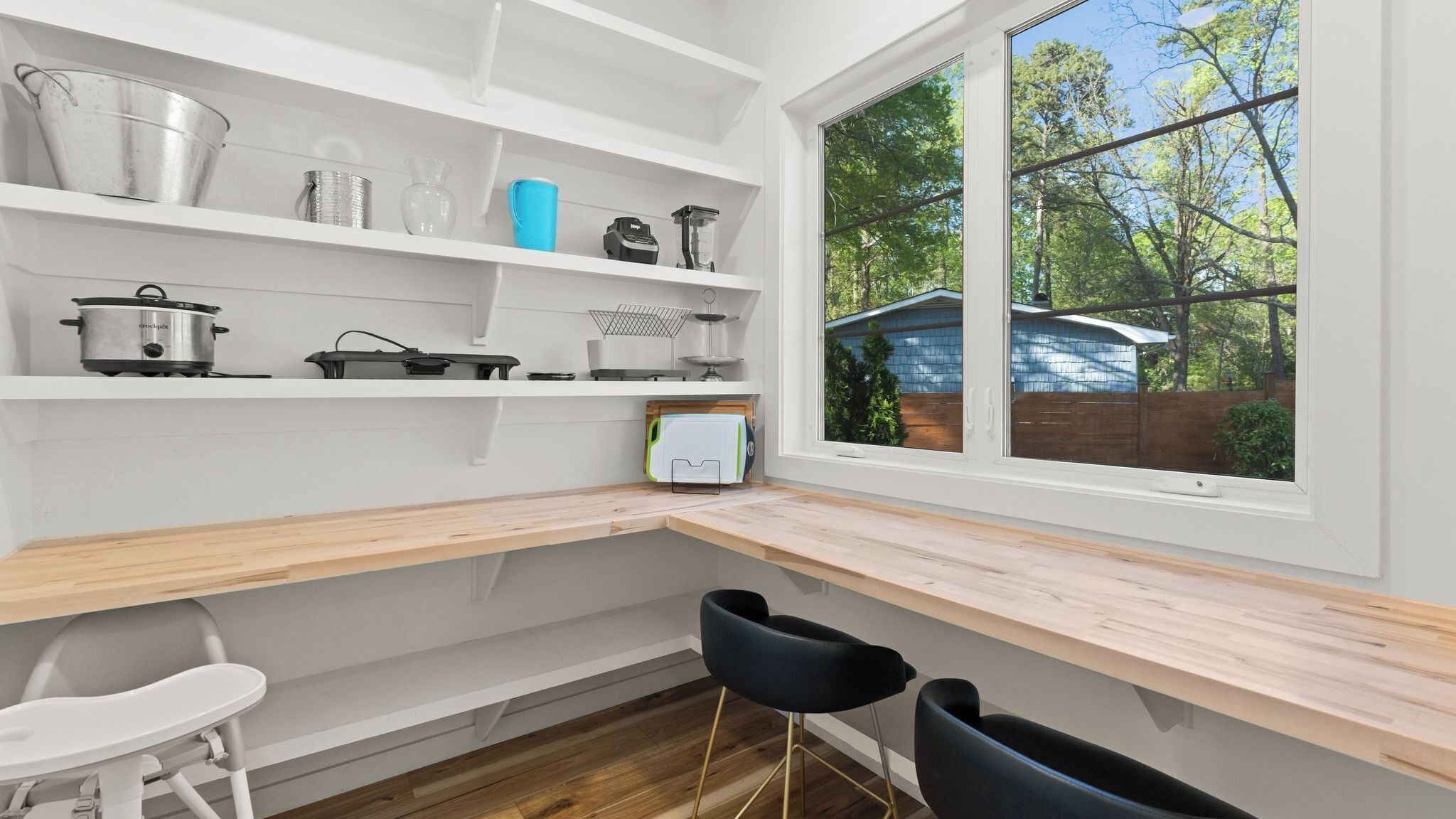 A modern kitchen with white cabinetry, a wooden countertop, and a window overlooking a backyard.