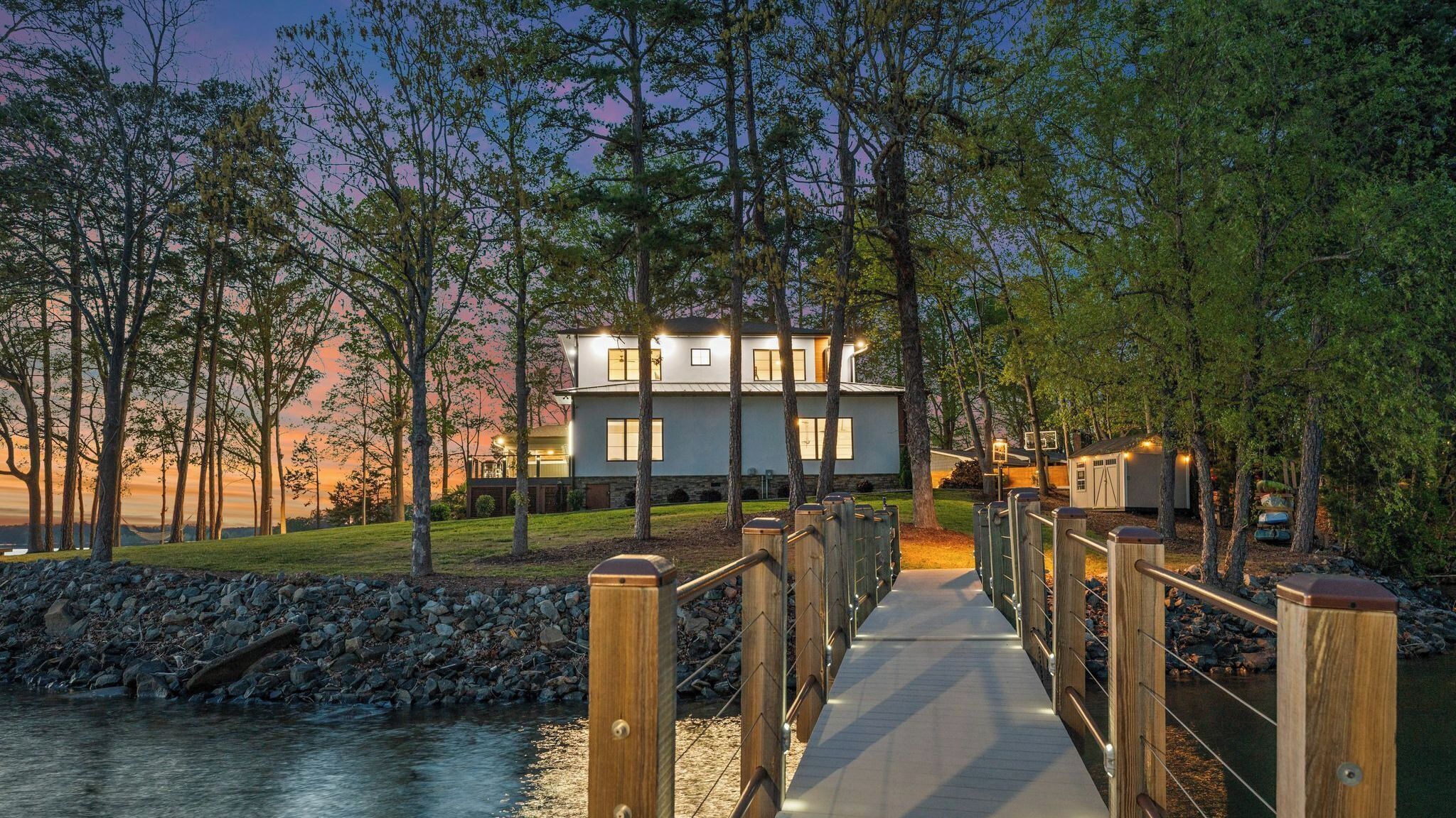 Uma casa moderna com um deck de madeira que dá para um rio, rodeada por árvores.