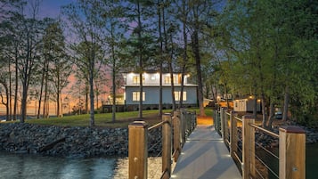 Uma casa moderna com um deck de madeira que dá para um rio, rodeada por árvores.