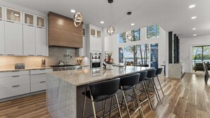 A modern kitchen with a large island, bar stools, and a view of the outdoors. - Paradise Peninsula by Avantstay Waterfront Private Beach, View (Mooresville)