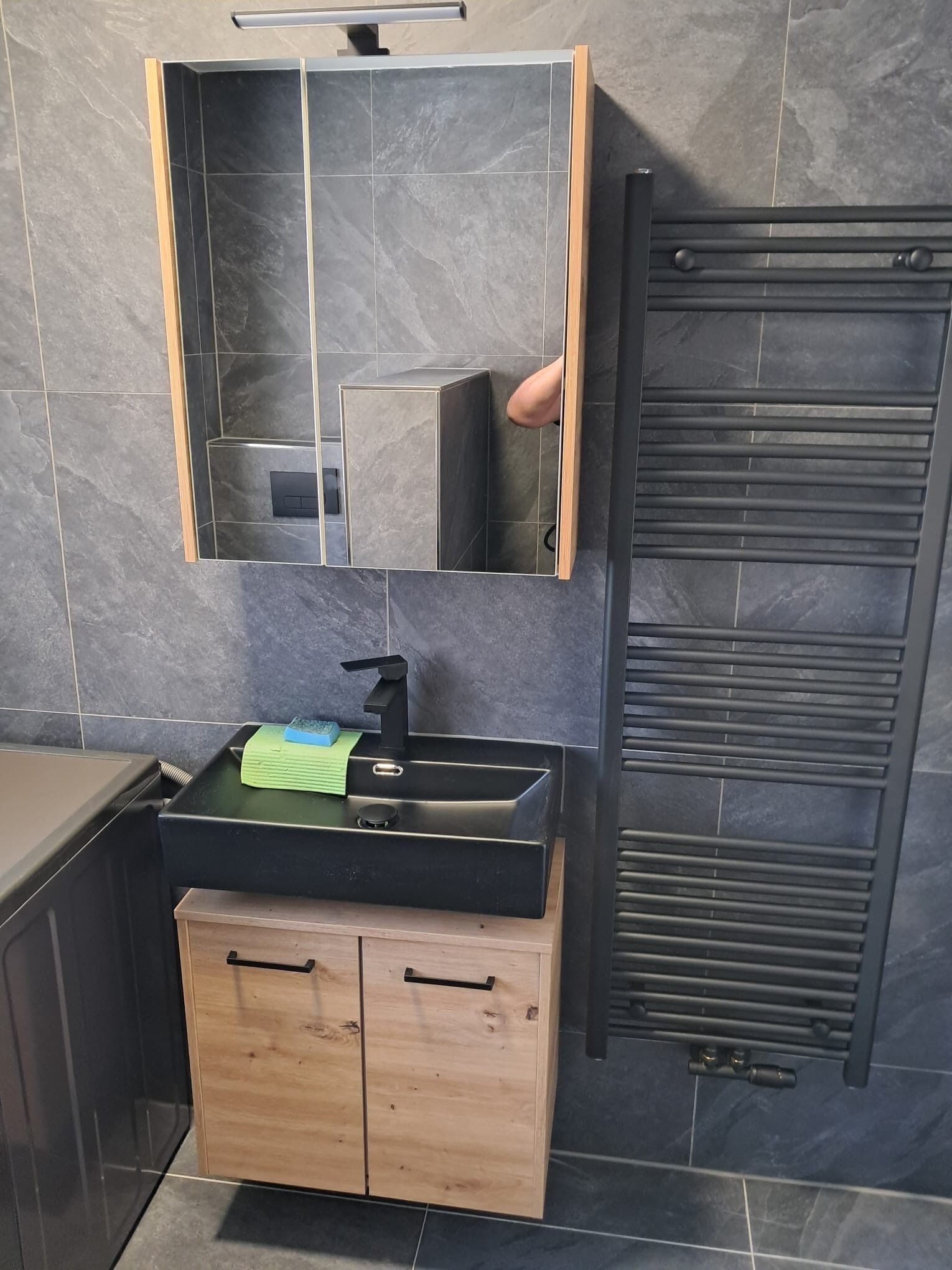Un baño con lavamanos negro, mueble de madera y perchero.