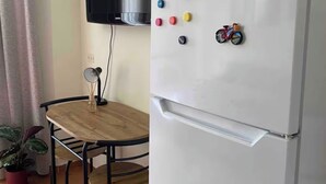 A compact kitchen with a white refrigerator, a small wooden table, a potted plant, and a mounted television. - Arena Stadium Apartment (Tiranë)