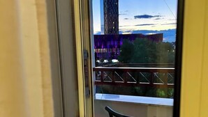 A balcony with a chair and a view of a building with purple lights. - Arena Stadium Apartment (Tiranë)