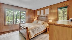 Um quarto com cama de madeira, janelas amplas e uma mesa de cabeceira.