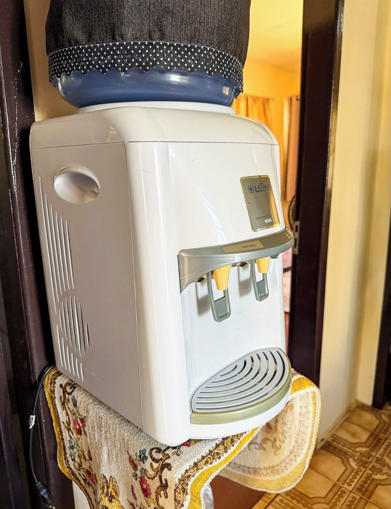 A vintage refrigerator with a water dispenser, placed on a patterned cloth.