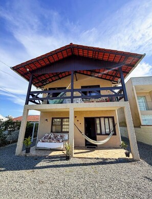 Una casa a due piani con tetto in tegole rosse, un balcone e un'amaca.