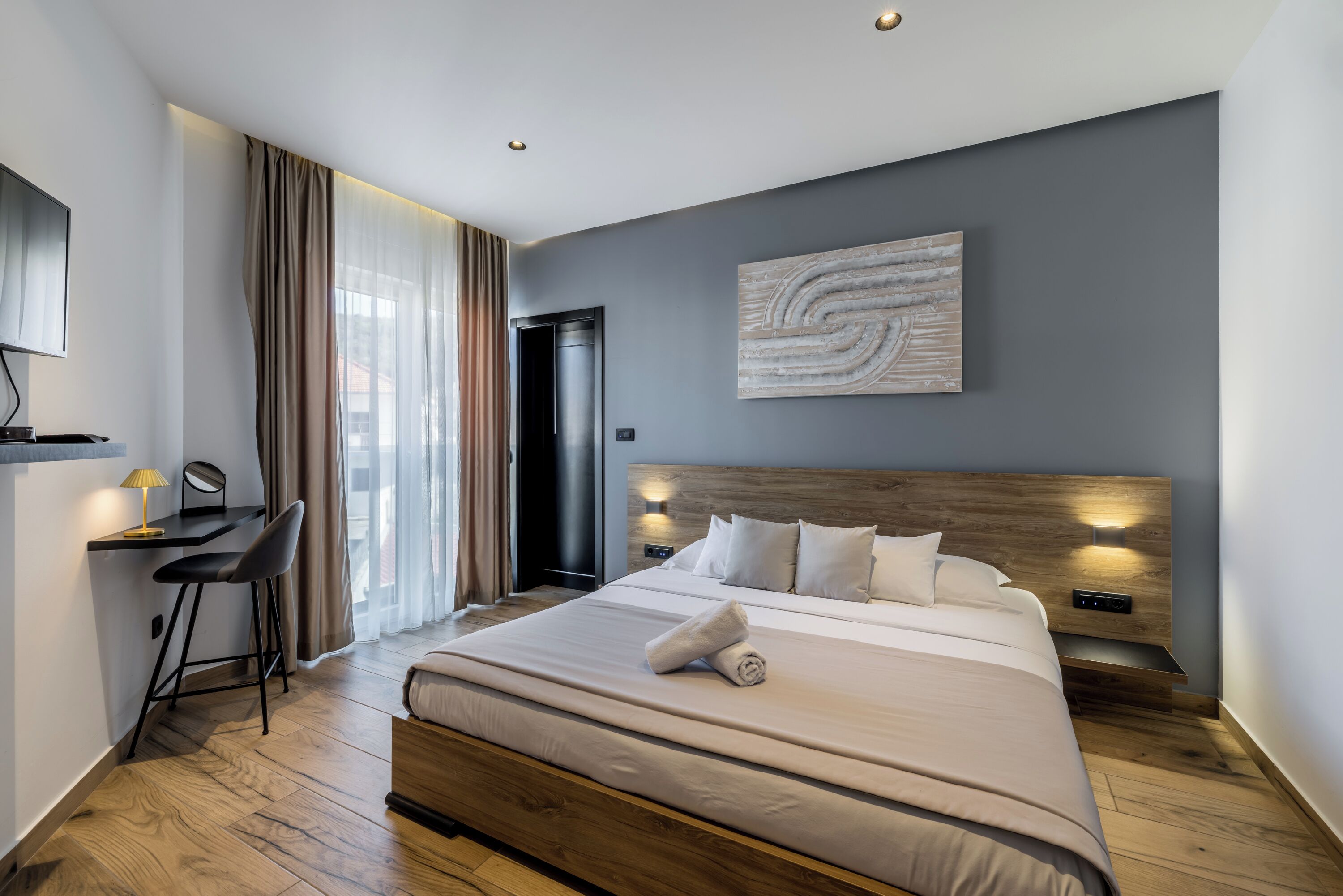 A modern hotel room with a large bed, a desk with a chair, a television, and a painting on the wall.