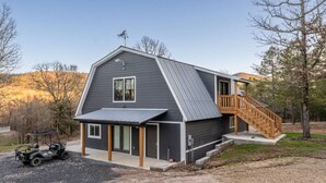 A two-story house with a sloped roof, a covered porch, and a staircase leading to an upper level. - Family Fun Barn - Pet Friendly (Hot Springs)