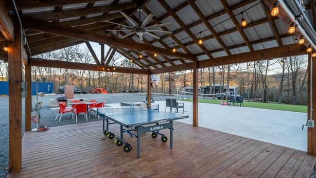 An outdoor covered area with a ping pong table, seating, and a ceiling fan. - Family Fun Barn - Pet Friendly (Hot Springs)