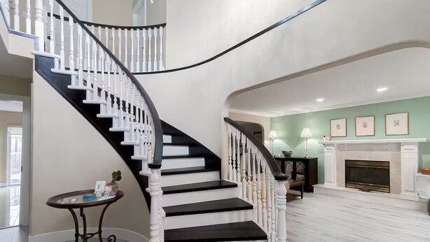 Eine prächtige Treppe mit weißen Balustraden und schwarzen Stufen, die zu einem Wohnbereich mit Kamin und grüner Wand führt.