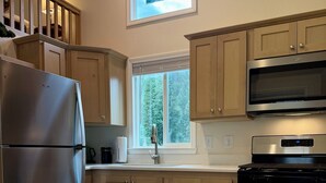 A modern kitchen with wooden cabinets, stainless steel appliances, and a window with a view of trees.