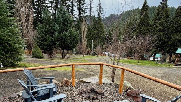 An outdoor seating area with Adirondack chairs and a fire pit, surrounded by a wooden fence and a gravel path.