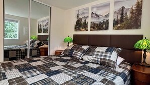 A bedroom with a large bed, a nightstand, a mirror, and three framed pictures on the wall.