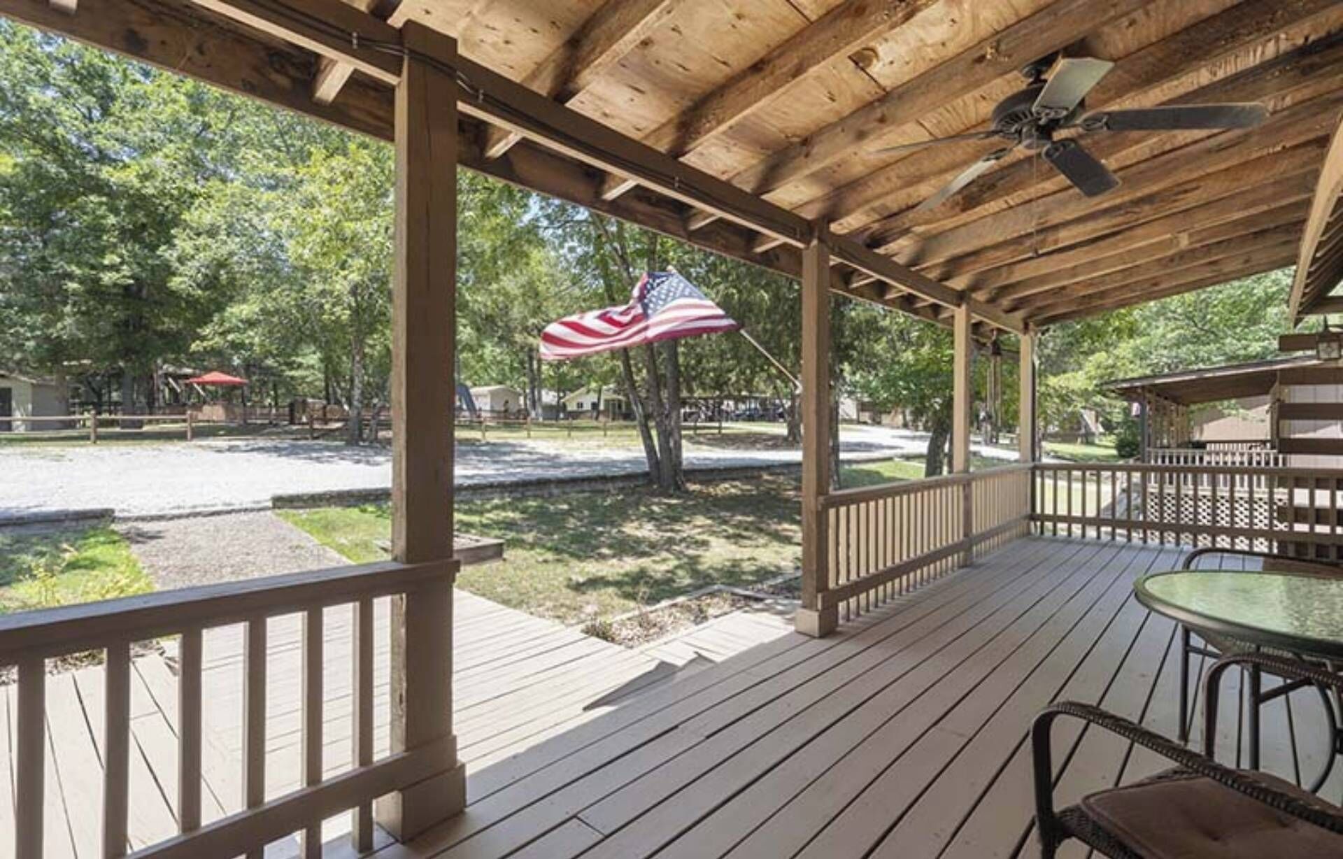 A covered outdoor area with a wooden deck, a table with chairs, and an American flag.