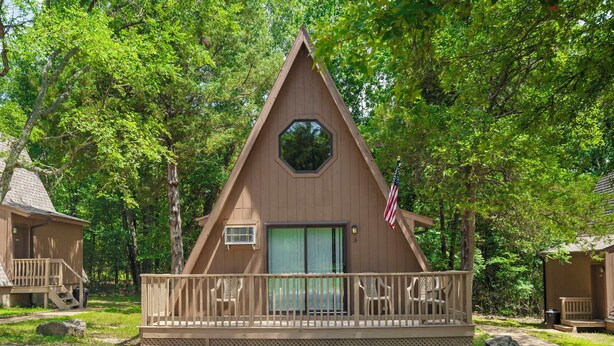 A cabin with a triangular roof, a deck with chairs, and an American flag. - One of our three large two bedroom “A” frame cabins at the Bar M Resort on Table Rock Lake (Branson)