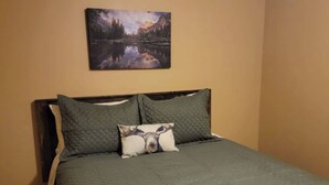 Una cama con un edredón verde y dos almohadas, una con un diseño de alce, en una habitación con un cuadro de un paisaje montañoso en la pared.