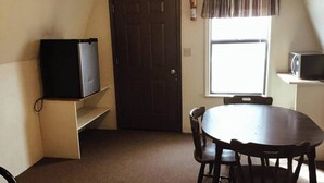 Una habitación pequeña con una puerta oscura, una ventana con vistas, una mesa con sillas y un televisor sobre una estantería.