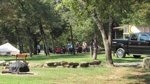 Un camping con tiendas de campaña, una parrilla cubierta y una camioneta pickup negra estacionada cerca.